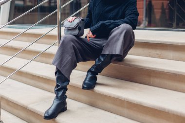 Sokak merdivenlerinde oturan şık ayakkabılar giyen, el çantası taşıyan bir kadın. Bahar modası kadın aksesuarları ve giysileri