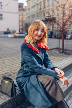 Mavi atkı takan şık bir genç kadının portresi şehir sokaklarında çanta çantasıyla rahatlıyor. Bahar modası kadın aksesuarları. Moda kıyafeti