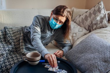 Ateşli Coronavirus gribi ya da soğuk algınlığı olan hasta kadın. Koruyucu maske takmış, evde su ve hap içen hasta bir kız. Pandemik karantina sırasında sağlık hizmetleri