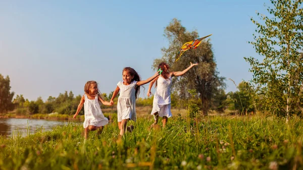 Mother\'s day. Happy girls running with kite in summer park while mother helps them. Children having fun playing outdoors. Family time