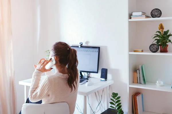 Work from home during coromavirus pandemic. Woman stays home talking on phone. Workspace of freelancer. Office interior with computer