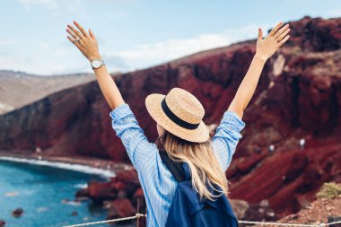 Akrotiri Santorini Yunanistan 'daki Kızıl Sahil manzarasına bakan bir turist. Sırt çantalı, kollarını kaldıran mutlu kadın gezgin.
