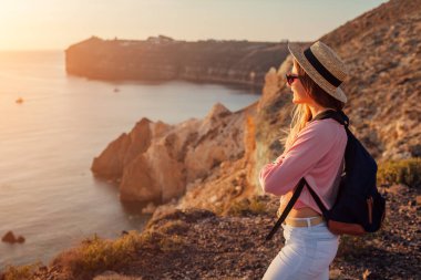 Yunanistan 'ın Ege Denizi Santorini adasındaki White Beach' teki dağda yürüyüş yapan gezgin manzaranın tadını çıkarıyor. Sırt çantalı kadın mutlu hissediyor. Yaz turizmi
