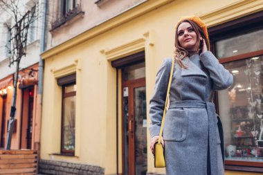 Açık havada sarı örülmüş gri bereli bir ceket giyen şık genç bir kadının portresi. Bahar modası kadın aksesuarları ve giysileri. Son moda klasik retro kıyafet.