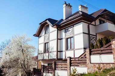 Baharda çiçek açan kahverengi çatılı ve erik ağacı olan beyaz kırsal İskandinav evi manzarası. Modern Avrupa mimarisi. Dış tasarım