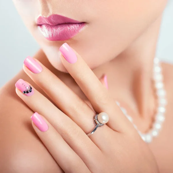 Nail art and design. Beautiful woman wearing make-up and pearl jewellery showing pink manicure with gems. Beauty fashion model. Skin care.