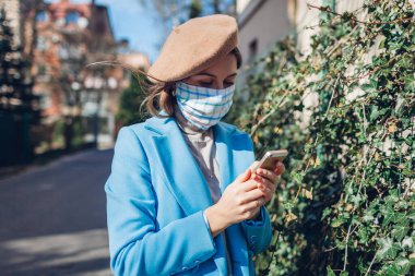 Coronavirus covid-19 salgını sırasında kadın açık havada tekrar kullanılabilir maske takıyor. Boş caddede akıllı telefon kullanan kız programları. Kendine dikkat et. Bahar modası