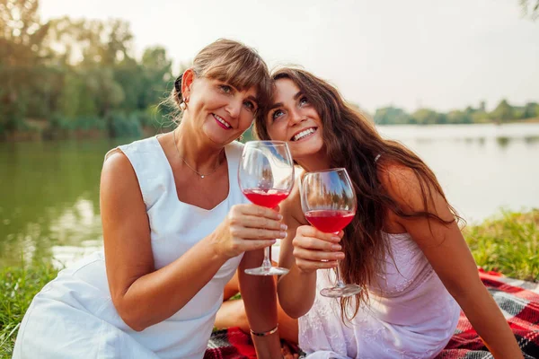 Mother's day. Mother drinking wine with her adult daughter in spring park. Family having picnic outdoors. Women spending time together