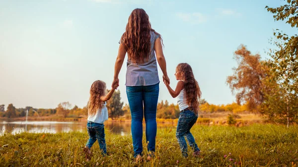 Family walking by summer river at sunset. Mother and her daughters having fun outdoors. Summer holidays