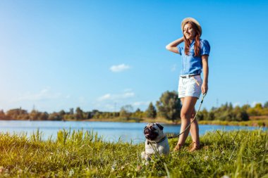 Bahar nehrinin kenarında oturan pug dog. Ustayla iyi yürüyüşler. Evcil hayvan ve kadın dışarıda takılıyor birlikte doğanın tadını çıkarıyorlar.