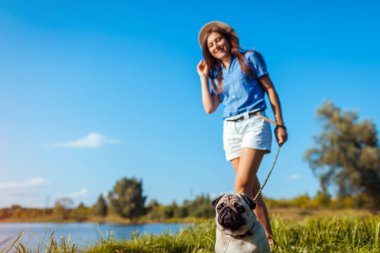 Bahar nehrinin kenarında oturan pug dog. Ustayla iyi yürüyüşler. Evcil hayvan ve kadın dışarıda takılıyor birlikte doğanın tadını çıkarıyorlar.