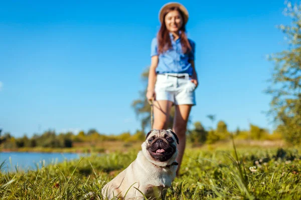 Bahar nehrinin kenarında oturan pug dog. Ustayla iyi yürüyüşler. Evcil hayvan ve kadın dışarıda takılıyor birlikte doğanın tadını çıkarıyorlar.
