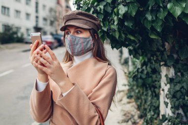 Şok edici bir haber. Kadın, Coronavirus covid-19 salgını sırasında boş caddede telefonla yeniden kullanılabilir el yapımı koruyucu maske takıyor. Panik