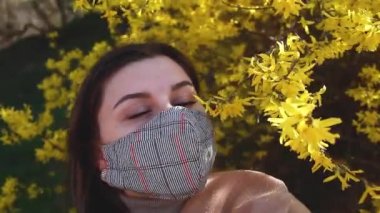 Coronavirus covid-19 salgını sırasında kadın dışarıda yeniden kullanılabilir el yapımı maske takıyor. Çiçek kokan bahçede çiçeklerin tadını çıkaran kız. Kendine dikkat et. Bahar modası