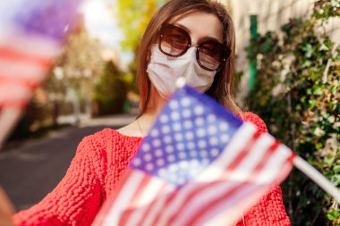 Kadın dışarıda koruyucu maske takıyor. 4 Temmuz 'da Amerika' nın Bağımsızlık Günü 'nü kutluyor. Coronavirus covid-19 pandemisi sırasında bayraklar taşıyor..