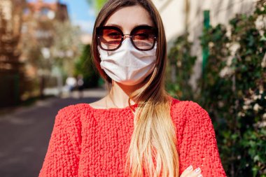 Kadın, Coronavirus covid-19 salgını sırasında dışarıda el yapımı koruyucu maske takıyor. Kız tek başına kameraya bakıyor.
