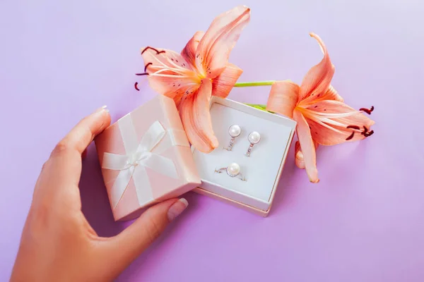 Woman opens gift box with set of pearl jewellery and flowers. Silver earrings and ring with lily. Gift present for holiday