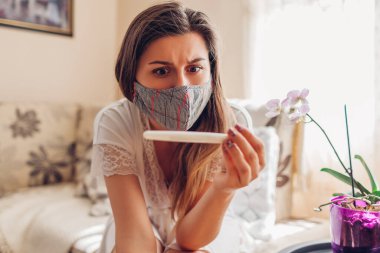 Coronavirus covid-19 salgını sırasında hamile kalmış. Koruyucu maskeli bir kadın evde hamilelik testi yaptırıyor. Şok olmuş ve korkmuş bir kız.