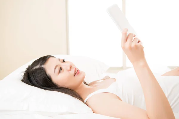 Mujer asiática leyendo con digital tablet dispositivo en cama — Foto de Stock