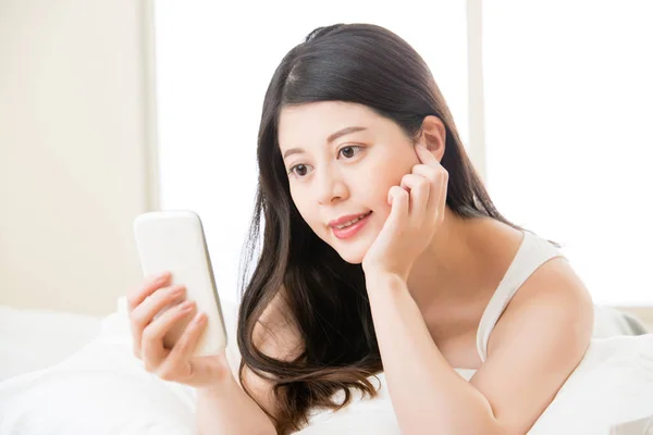 Joven sonrisa asiática mujer leyendo smart phone en cama — Foto de Stock