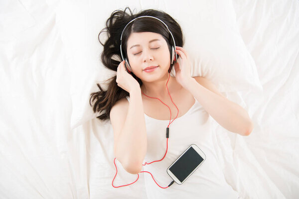 asian woman enjoy music by smart phone with headphones. bed