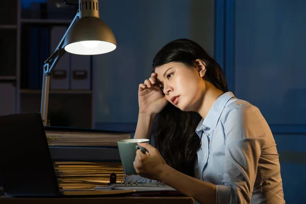 Азіатська бізнес жінка п'є каву освіжаючу працюючи понаднормово la — стокове фото