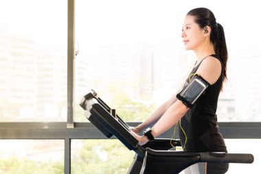 Güzel Asyalı kadın koşma koşu bandı kullanım akıllı telefon dinleme.
