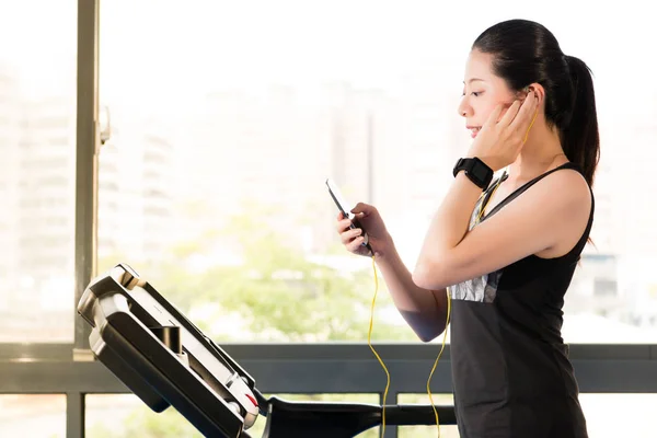 Linda mulher asiática correndo esteira usar smartphone ouvindo — Fotografia de Stock