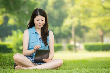 Güzellik Asyalı kadın çimenlerin üzerinde oturan dijital tablet kullanma