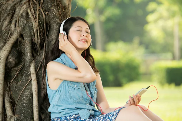Hermosa asiático mujer escuchar música sentado en hierba — Foto de Stock