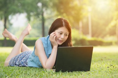 çimenlerin üzerinde bilgisayar kullanan güzel Asyalı kadın