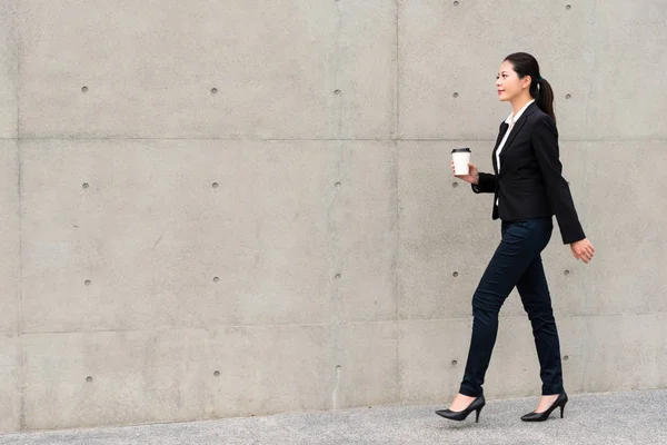 Elegante gerente mujer caminando en gris pared —  Fotos de Stock