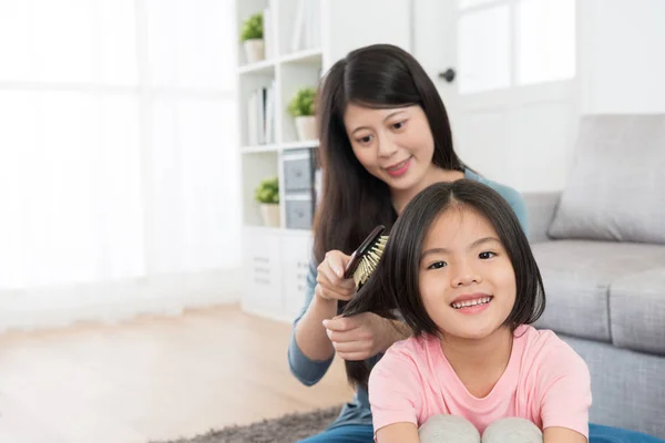Χαμογελώντας όμορφη μητέρα χρησιμοποιώντας πινέλο χτενίζει τα μαλλιά — Φωτογραφία Αρχείου