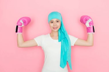 Boks pembe arka planda duran ve güçlü kas kameraya bakarak gösterilen eldiven giymiş mutlu kendine güvenen kadın kanser hastası.