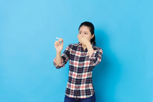 Senhora segurando cigarro de pé no fundo azul — Fotografia de Stock