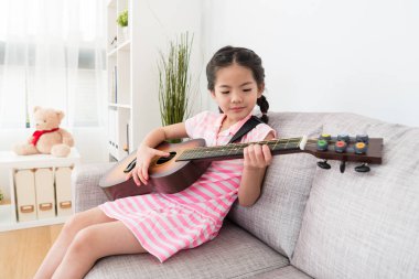 Kız kanepede gitar çalıyor.