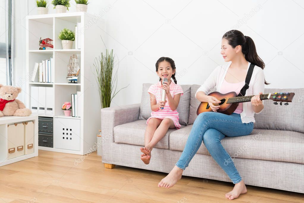 Mom plays guitar daughter sing on the sofa.