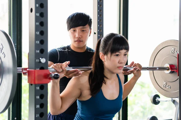 Coach insure girl while squats with barbell — Stock Photo, Image