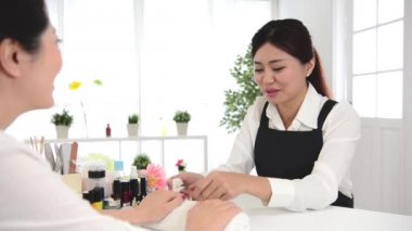 Profil görünümü bir genç ve güzel karışık Asyalı kadınların manikür zevk ve onun manikürcü, gerçek salon spa arka plan ile konuşuyor. Güzellik ve moda kavramı.
