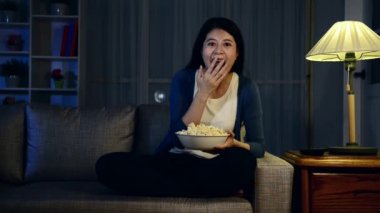 komik ilginç program ve geceleri patlamış mısır yemeyi paylaşımı işaret izlerken oturma odası kanepe kanepede oturan mutlu güzel kadın.