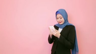 Kendine güvenen güzellik Müslüman Ofis Yöneticisi kadın manifatura iletisi pembe arka planda duran ve kamera gülümseyen seyir telefon smartphone ile iş için.