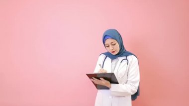 profesyonel zarif kadın Müslüman doktor hasta tıbbi kayıt kişisel noteboard pembe duvar arka plan üzerinde izole yazma.