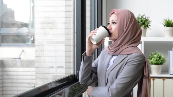 美しさが魅力的女性イスラム教徒のビジネス ワーカー事務所に立って 空想リラックス外のウィンドウを見て コーヒーのマグカップを保持 — ストック動画