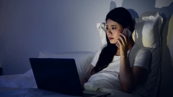 美しいビジネス女性夜遅く自宅のベッドの上の作業コンピューターを使用して顧客から電話呼び出しに応答します — ストック動画