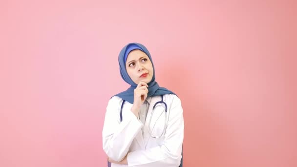ピンクの背景に分離されてかなり魅力的なイスラム教徒の女性医師思考医療業務ソリューション — ストック動画
