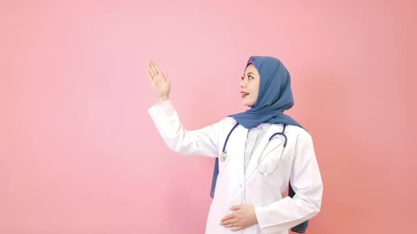 かなりエレガントな女性イスラム教徒の病院医師を提示姿勢とピンク背景のカメラ目線に立って — ストック動画