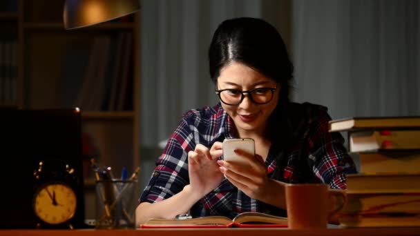 美しい若い学生机に座って宿題をして夜遅くまで残業で彼女の友達を自宅にスマート フォンのテキスト メッセージを使用して — ストック動画