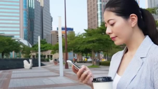 携帯電話スマート フォン アプリのテキスト メッセージと通りを歩いてコーヒーのカップを持っている手を使用して若いアジア女性実業家 — ストック動画