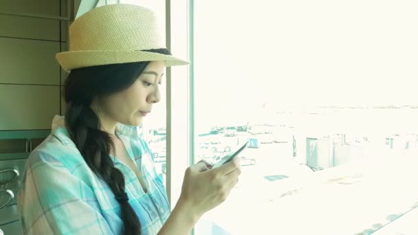 荷物テキスト メッセージと立っている旅行観光は空港ウィンドウでメッセージを読みます 出発前に搭乗口で待っている間飛行機を見てラウンジで待つ女 — ストック動画