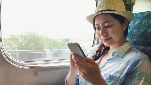 アジアの女性の鉄道で旅行スマート フォン アプリ テキスト メッセージを使用して 旅行休暇に輸送中にビデオ保有携帯電話を見て幸せな若い女性 — ストック動画